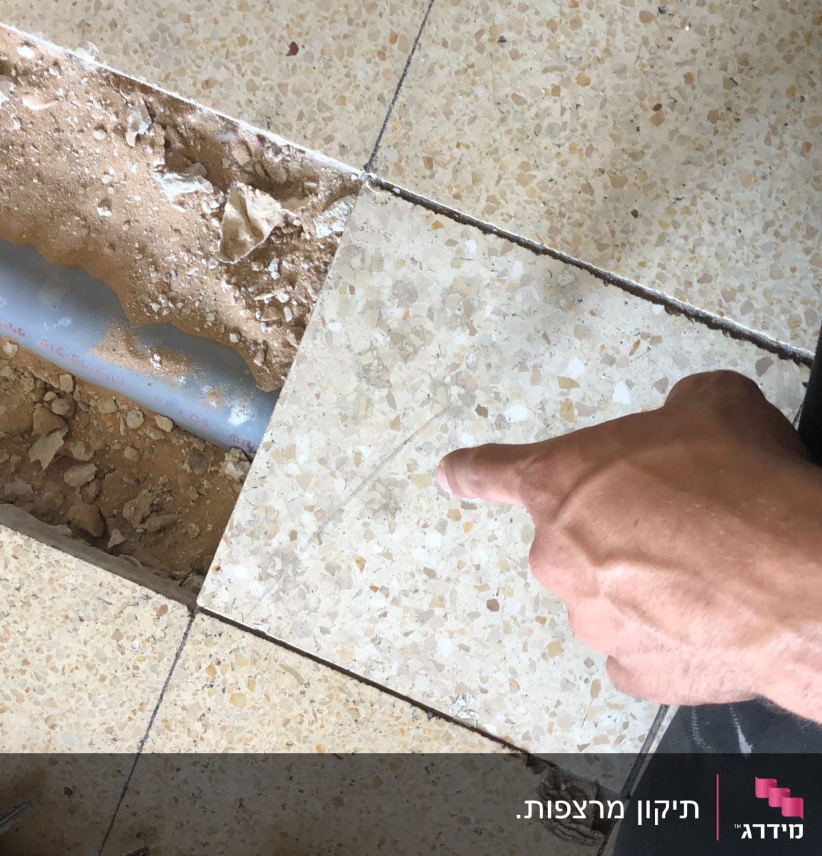 יד מצביעה על צינור מתחת לרצפה שבורה